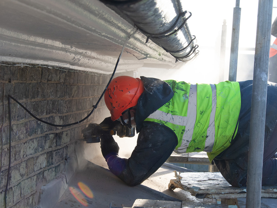 Workman using grinder with hard hat and respirator