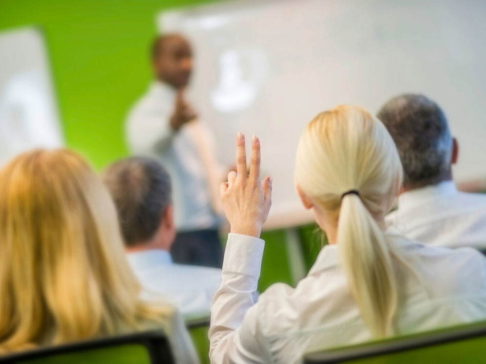 Person raising hand during seminar and lecturer pointing at them to ask their question