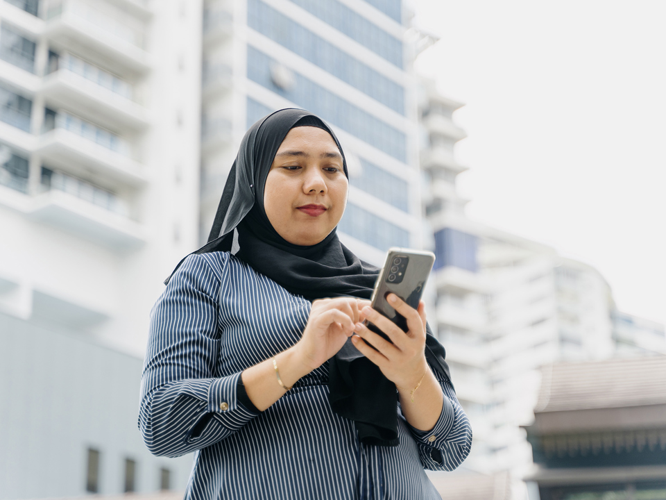 Woman in headscarf using tablet computer outside tall white building